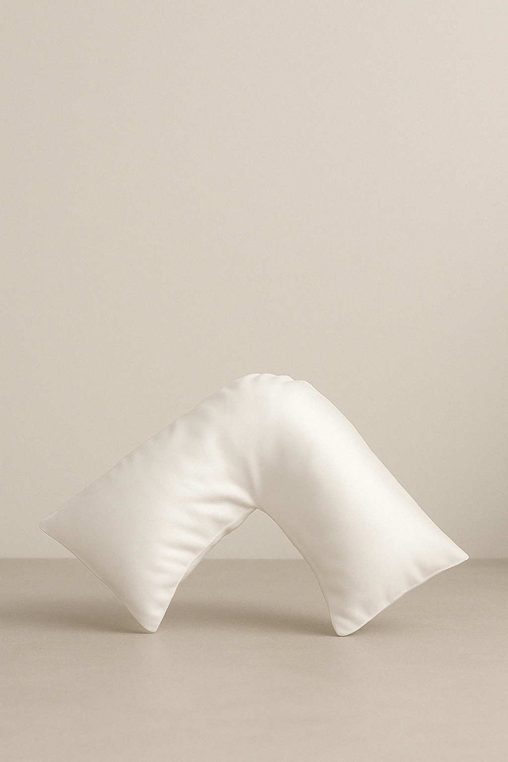 An ivory silk pillowcase with a unique curved shape designed for beauty sleep, placed against a neutral background. – Ivory